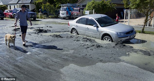 Destruction: A dog walker looks at a car trapped in a sink hole caused by liquefaction in the Christchurch suburb of Parklands following the earthquake