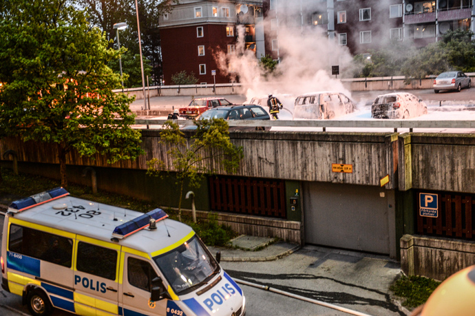 Policemen extinguish burning cars after youths rioted in Husby, northern Stockholm on May 20, 2013 (AFP Photo / Fredrik Sandberg / Scanpix Sweden/ Sweden out)